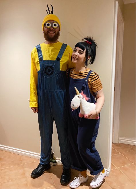 Two people in costumes. One is wearing a minion costume. They have a yellow beanie with black pipe cleaners stuck on, a yellow and blue overall costume and black boots he is wearing minion eye goggles. The girl has her hair tied in a high pony tail with a red scrunchie. She’s wearing a yellow shirt with navy stripes and blue cloth overalls. She has yellow socks and white converse sneakers on and she’s holding a plush white unicorn. They are both smiling Dispicle Me Costumes, Minions Couple Costume, Minion Couple Costume, Halloween Costumes For Families, Despicable Me Halloween Costume, Agnes Costume, Adult Minion Costume, Despicable Me Costume, Partner Halloween Costumes