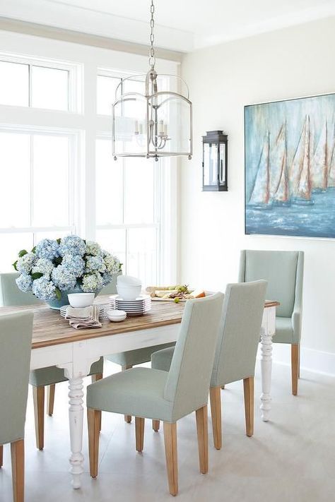 Large dining room windows invite lots of light shining on a white dining room table with a wood top embellished by blue floral arrangements. White Dining Room Table, Collection Decor, Coastal Dining Room, Dining Room Windows, Beach House Interior Design, Coastal Room, White Dining Room, Coastal Living Rooms, Beach House Interior