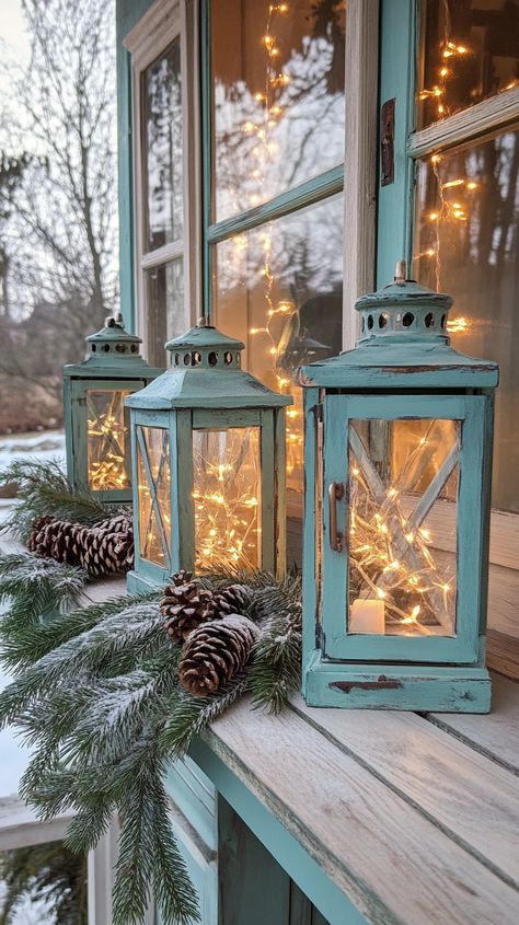 Rustic lanterns with fairy lights on a wooden windowsill, surrounded by evergreen branches and pine cones in muted teal and Wooden Windowsill, Woodsy Farmhouse, Candle Centerpieces Elegant, Decorating With Lanterns, Rustic Candle Centerpieces, Lantern Aesthetic, Rustic Christmas Decor Ideas, Muted Teal, Birch Candles