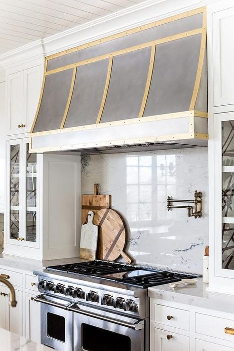 Exquisite kitchen features a steel kitchen hood accented with brass trim which stands over a marble cooktop backsplash lined with a swing arm pot filler and a stainless steel stove with dual ovens flanked by glass door cabinets with backs of shelves lined with black and white abstract wallpaper, Kelly Wearstler Channels Wallpaper. Kitchen Hood Ideas, White Kitchen Traditional, Oven Hood, Kitchen Vent Hood, Kitchen Vent, Kitchen Range Hood, Kitchen Hoods, Gold Kitchen, Kitchen Stove