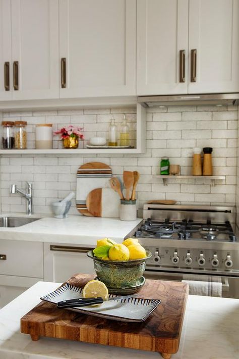 Small kitchen designed with a small range and a steel shelf above the stove mounted on white brick tiles under cream cabinets finished with vintage brass hardware. Shelf Above Stove, Kitchen Trends 2020, White Brick Tiles, Stove Hood, Stainless Steel Shelf, Top Kitchen Trends, Cream Cabinets, Small Stove, White Marble Countertops