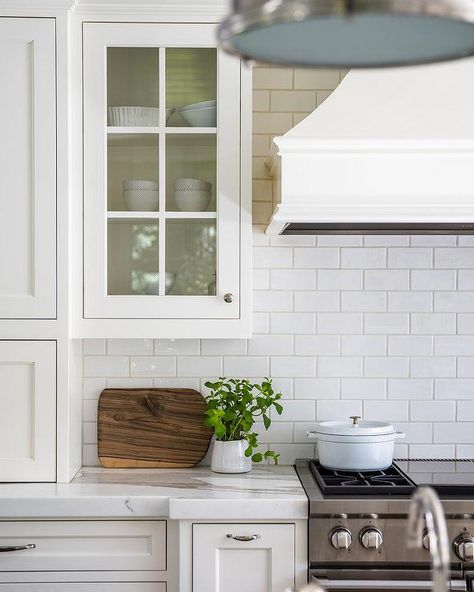 Kitchen features white subway tiles with ivory grout, glass front white cabinets with nickel pulls and a white French paneled range hood over a Wolf dual range. White Subway Tile With Accent Above Stove, Subway Tile Brown Grout, Cream Subway Tile, Brown Grout, White Subway Tiles, White Subway Tile, Subway Tiles, Transitional Kitchen, Kitchen Features