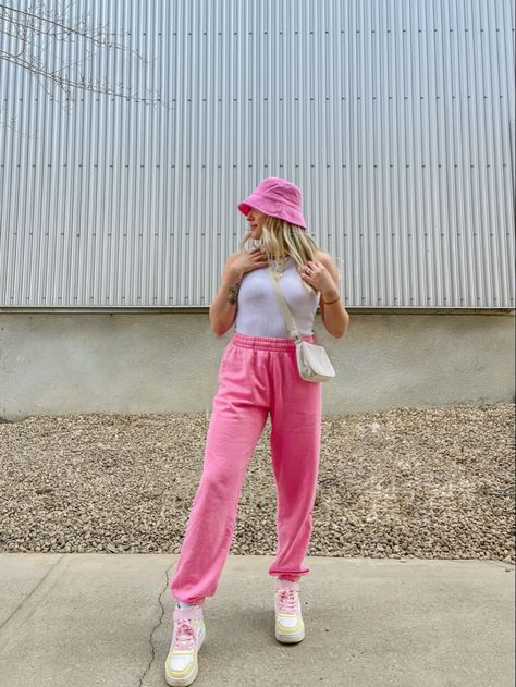 Girl standing up posing looking away from the camera. She is wearing pink sweat pants, a white bodysuit, a pink bucket hat, pastel coloured shoes and a white cross body bag. Outfits With Pink Joggers, Pastel Sweatpants Outfit, Pink Sweat Pants Outfits, How To Style Pink Sweatpants, Pink Track Pants Outfit, Pink Bucket Hat Outfit, Outfit Ideas With Sweatpants, Pink Joggers Outfit, Pink Sweats Outfit