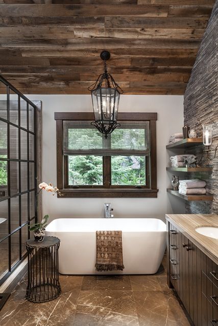 A vintage light from Paris hangs above the tub in the master bathroom, which is accented by a side table from Formations. The iron and glass shower enclosure was custom designed. The shade fabric is from Schumacher. Cabin Bathrooms, Bad Inspiration, Rustic Bathrooms, Rustic Bathroom, Cool Ideas, Style At Home, Bathroom Remodel Master, House Bathroom, Beautiful Bathrooms