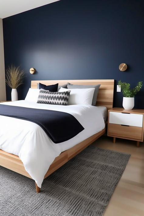 Photographed from an angle that captures the entire king-size bed and most of the room, this modern bedroom features a midnight blue accent wall balanced by light wood tones. A wooden headboard, matching nightstands, and a neutral area rug complete the look. Blue Feature Wall Bedroom, Midnight Blue Bedroom, Dark Blue Rooms, Dark Blue Bedrooms, Blue Bedroom Walls, Feature Wall Bedroom, Blue Accent Walls, Boho Bedroom Design, Dekorasi Kamar Tidur