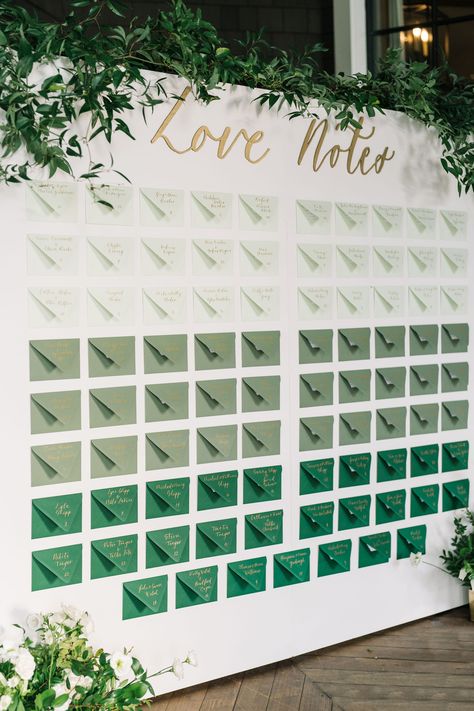 A green seating chart for wedding reception with greenery and flowers surrounding it. Perfect for a wedding that has green in their color palette. The couple wrote a note to each guest. Creative Table Seating Chart Wedding, Wedding Seating Assignment Display, Matches Seating Chart, Emerald Seating Chart, Wedding Favors Seating Chart, Reception Seating Chart Layout, Big Wedding Seating Chart, Wedding Seating Chart With Gift, Thank You Note Seating Chart