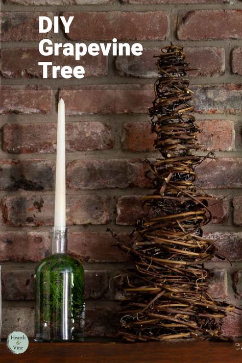 A cone shaped tree made from grapevines sits on a mantle with a bottle and candle. Things To Make With Grape Vines, Hanging Grapevine Wreath From Ceiling, Grapevine Trees Diy How To Make, Grapevine Craft Ideas, Grapevine Garland Christmas Tree, Crafts With Grape Vines, Grapevine Christmas Trees, Grapevine Garland Front Door Christmas, Grapevine Swag Ideas