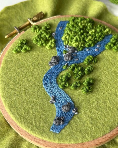 This piece was going to be a part of the flower bush collection, but I’ve decided to take it in a different direction. I was originally inspired by rivers in the amazon that split and wind with trees surrounding them. As I added rocks to the river, and decided on 2-3 different shades of foliage, I started to see the piece as a more detailed amazon themed one instead of decorated with beads. I plan to add more rocks, maybe some dried grass too. We’ll just see where this piece goes 🌿 . . . #emb... Bush Embroidery, Grass Embroidery, Golden Rod Embroidery, Embroidery Nature Scene, River Textile Art, Wool Felt Projects, Vintage Embroidery, Hoop Art, Felting Projects