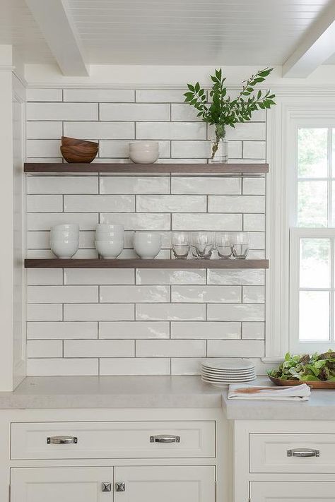 Gorgeous white kitchen boasts dark stained floating shelves mounted on linear backsplash tiles under a beadboard ceiling and beside a window fixed above white shaker cabinets adorning polished nickel hardware and a carrera marble countertops. White Subway Tile Kitchen, Gorgeous White Kitchen, Subway Tile Backsplash Kitchen, Subway Tile Kitchen, Kitchen Backsplash Designs, Kitchen Splashback, White Subway Tile, Metroid, Kitchen Tiles Backsplash