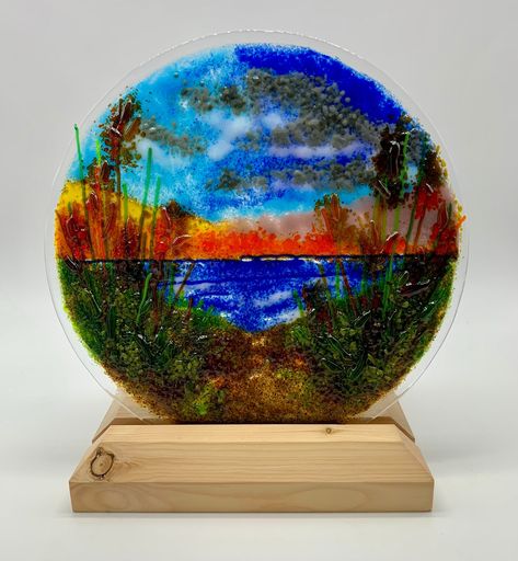 Introducing a captivating 9-inch Glass Fused Ocean Sunset Oasis. This circular masterpiece transports you to the serene beauty of an ocean sunset beach, capturing the warm hues of the sinking sun against the tranquil backdrop of sandy dunes and swaying beach grass. Meticulously crafted, this piece embodies the essence of coastal serenity, with each element - from the sun-kissed waves to the gentle rustle of beach grass - carefully fused into a harmonious composition. The circular design adds a sense of fluidity, enhancing the immersive experience of a peaceful seaside retreat. Please note that the display stand is not included, allowing you the freedom to choose one that perfectly complements your personal style. Whether adorning a tabletop or hung on a wall, let the Glass Fused Ocean Suns Fused Glass Sunset, Beach Grass, Glass Fusion, Christmas Lanterns, Circular Design, Ocean Sunset, Art Beach, Fused Glass Art, Glass Art Sculpture