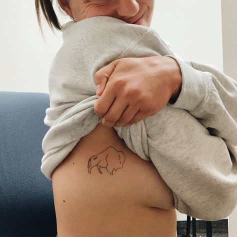 Picture of a tattoo on the side of a girl’s rib cage. Tattoo is a silhouette of a Buffalo with a 716 on the Buffalo’s lower back Minimalist Bison Tattoo, Buffalo Bills Tattoo Ideas, 716 Tattoo, Buffalo Tattoo Feminine, Buffalo Tattoo Ideas, Buffalo Bills Tattoo, Bison Tattoo, Golden Tattoo, Buffalo Tattoo