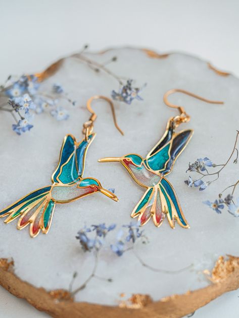 A pair of beautiful blue hummingbird earrings inspired by stained glass compositions.  Each of these bird earrings' holes is filled with different resin tones, creating a beautiful aesthetic, which makes this hummingbird jewelry so magical and colorful. You can choose the handmade earrings' tone from two different tones, gold, and silver. ✦ MEASUREMENT bird pendant: 40 X 20 mm ✦ DETAILS The bird pendants are made of gold or silver-plated stainless steel. The earring hook is hypoallergenic. You c Handpainted Earrings Clay, Stainless Glass Art, Magical Jewelry Pendants, Hummingbird Aesthetic, Stain Glass Jewelry, Magical Earrings, Bird Earring, Blue Hummingbird, Hummingbird Jewelry