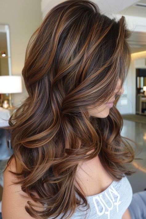 Woman with long, wavy brown hair with highlights styled in loose curls. Carmel Full Highlights On Brown Hair, Medium Brown With Caramel Balayage, Dark Brown Hair With Caramel Highlights Layers, Cool Toned Lowlights For Brunettes, Chocolate Brown Hair Caramel Balayage, Carmel Highlights On Brunette Hair, Caramel Highlights With Curtain Bangs, Colored Highlights In Dark Brown Hair, Layered Dark Hair With Highlights