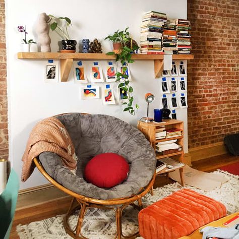 A plush gray papasan chair on a wooden frame, inside an artful bohemian apartment with a brick wall, stacks of books, and small pieces of artwork taped to the wall Small Bohemian Apartment, Papasan Chair Bedroom, Papasan Chair Living Room, 2020 Bedroom, Design Intervention, Bohemian Apartment, Apartment Things, Modern Furniture Design, Cozy Rooms