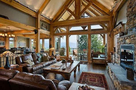 Expansive windows bring lots of light into the great room, which is open and airy with the vaulted ceilings and timber frame trusses . Hybrid Timber Frame Homes, Timber Frame Great Room, Timber Frame Home Plans, Timber Trusses, Timber Truss, Stone Fireplace Surround, Timber Frame Home, Timber Frame House, Timber Frame Homes