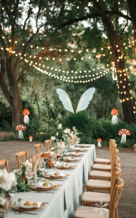 An outdoor dining setup perfect for baby shower ideas features a long table with white tablecloths, elegantly arranged tableware, and floral centerpieces. String lights hang above, while large butterfly wings add whimsy to the enchanted forest theme amidst mushroom decorations and lush greenery. Fairy Gender Reveal, Fairy Tale Baby Shower Ideas, Enchanted Forest Baby Shower Theme Girl, Fairytale Baby Shower Ideas, Fairy Baby Shower Theme, Enchanted Forest Theme Baby Shower Ideas, Enchanted Garden Baby Shower Theme, Fairy Baby Shower Ideas, Forest Themed Baby Shower Ideas