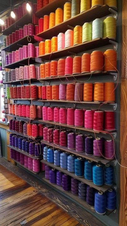 A vibrant selection of colorful thread spools organized neatly on shelves in a crafter's paradise. Fabric Swatches Storage, Bobbin Thread Storage, Textile Showroom, Cotton Reel Holders Thread Storage, Thread And Bobbin Storage, Large Thread Spool Storage, Vintage Sewing Kit, Sewing Nook, Fashion Atelier