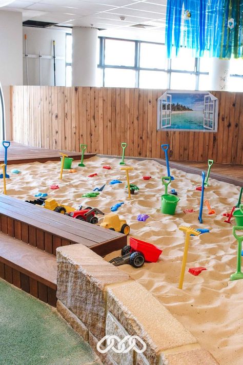 Sandpit with coloured toys, trucks, and wooden fence and steps. Montessori School Playground, Childcare Centre Design, Childcare Center Lobby, Montessori Playground Ideas, Play Centre Ideas, Sandpit Ideas Childcare, Day Care Activity Ideas, Indoor Sandpit, Children’s Museum