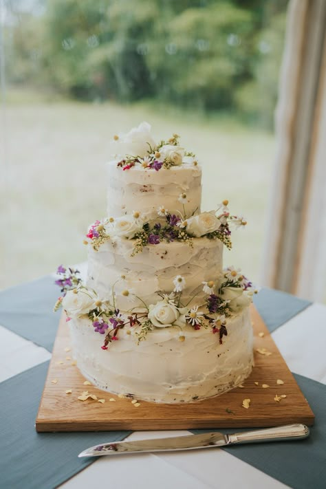 Three tier rustic white iced wedding cake with daisies and roses at marquee wedding Tiered Carrot Cake, Small Two Layer Wedding Cake, Flowery Wedding Cakes, Meadow Wedding Cake, Wedding Cake Wild Flowers, Simple Wedding Cake Ideas 2 Tier, Wedding Cake Wildflowers Simple, Real Flower Wedding Cake, Wedding Ice Cream Cake