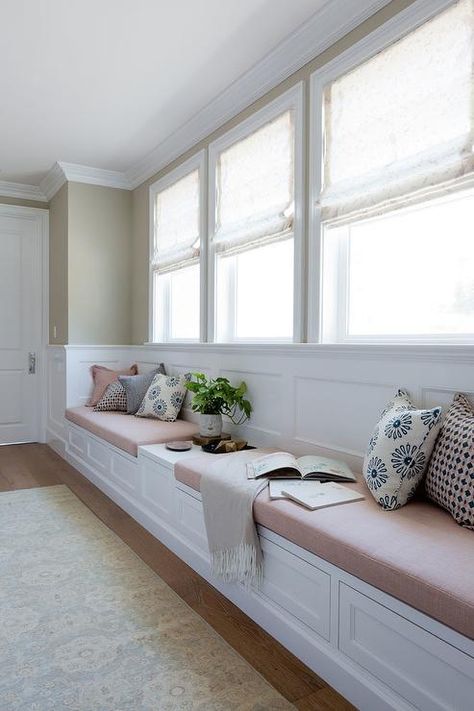 A cream colored rug sits in front of a long built-in white window seat fitted with drawers and blush pink linen cushions flanking a built in table fixed against a wainscot backsplash beneath three windows dressed in natural linen roman shades complementing tan upper walls. Long Window Seat, Bedroom Window Seat, Wainscoting Kitchen, Window Seat Kitchen, Wainscoting Bedroom, Window Seat Design, Wainscoting Styles, Closet Built Ins, Sala Grande