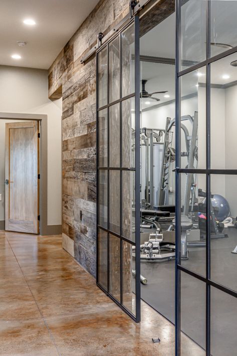 Whatever kind of room you want in your home, we'll design it! We love these glass barn doors leading into this client's awesome home gym. This room is where functional meets modern, and we are obsessed! ID.ology Interiors & Design can make all of your home dreams come true. We are based out of (but not limited to) Asheville, NC. Check out our website to learn more! Glass Gym Room, Glass Wall Gym Design, Basement Gym Glass Walls, Gym With Glass Doors, Basement Gym Door Ideas, Basement Gym Doors, Rustic Workout Room, Basement Gym Glass Door, Modern Home Gym Interior Design