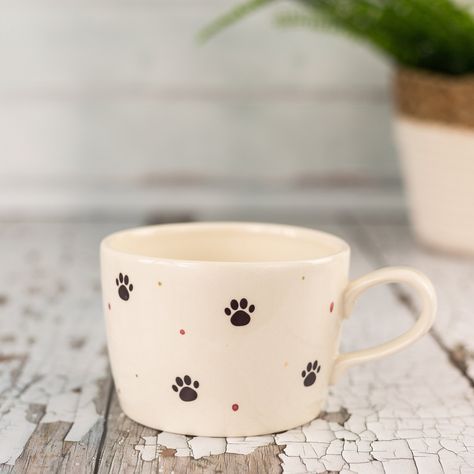 Decorated with cute paw prints (there's even one in the bottom of the cup) and hand painted pink and gold metallic spots, our stoneware cups are the perfect shape and size for cosily cupping in two hands. Our cups come snugly packed in a branded gift box. ceramic stoneware. The metallic lustre used for the spots contains real precious metal and therefore isn't suitable for microwave use. Dishwashing will scratch and dull the lustre so we recommend washing by hand. Height 7.8cm, diameter 10.cm, 1 Coffee Cup Painting Ideas, Paint A Mug Ideas, Pottery Painting Designs Mugs, Painting Cups Ideas, Dog Mug, Mug Design Ideas, Handmade Mug, Mug Painting, Painted Mug