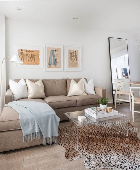 Welcoming living room boasts three framed vintage pattern art pieces mounted to a white wall above a taupe sofa with a chaise lounge accented with champagne metallic pillows, white pillows, and a light blue throw blanket, while a CB2 Peekaboo Acrylic Coffee Table sits in front of the sofa on a cheetah print cowhide rug. Taupe Couch, Beige Couch Living Room, Farmhouse Beige, Taupe Sofa, Rugs Beige, Beige Couch, Couch With Chaise, Livingroom Layout, Living Room Inspo