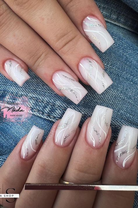 These almond-shaped nails boast an elegant design with a soft pink base that transitions seamlessly into white tips. The nails feature a subtle marble effect created with delicate white lines swirling over the surface. Sparkling silver glitter traces the curving patterns, adding a touch of glamour to this sophisticated look. Perfect for those who love a chic and polished appearance.  // Photo Credit: Instagram @nadanailart White Nails With Silver Lines, White And Silver Nails Designs, Medium Ballerina Nails Designs, Nail Designs With Swirls, White Nails With Lines, White Base Nails With Design, Nails With Glitter Lines, White Silver Nail Designs, Nude Marble Nail Designs