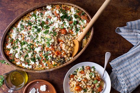 Baking pearl couscous with chickpeas, roasted tomatoes and garlic results in a one-pan vegetarian meal that’s cozy and very savory, especially if you use a flavorful stock for cooking Soft and almost porridgelike in texture, it satisfies the same urge as polenta or risotto Lemon zest and fresh herbs make it bright, while feta, added at the end, gives the whole thing a creamy richness Pearl Couscous, Creamy Feta, Gratin Dish, Meatless Mondays, Chickpea Recipes, Tomato Vegetable, Nyt Cooking, Vegetarian Meals, Spaghetti Squash