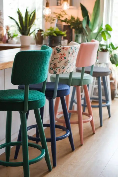 Colorful bar stools lined up in a cozy, plant-filled kitchen. Mismatch Barstools, Mix Match Bar Stools, Breakfast Bar Seating, Colorful Bar Stools Kitchen Island, Upholstered Counter Stools With Backs, Kitchen Stools For Island, Bar Stool Ideas, Kitchen Counter Seating, Comfy Bar Stools