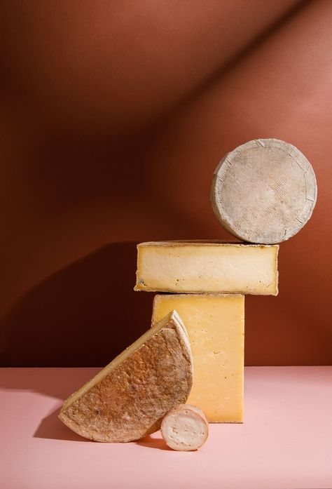 Stack of large cheeses balanced on top of one and other. Background is chestnut brown and pink Food Still Life Photography, Jack Spicer, Creative Food Photography, Cheese Festival, Food Still Life, Cheese And Wine, Spanish Modern, Wine And Cheese, Cheese Shop