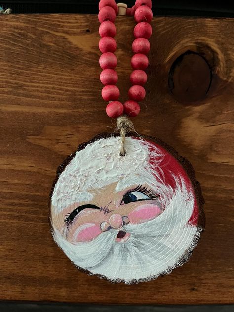 An original painting of a winking Santa Claus on a 3"-3.5" wood slice. Strung on twine with hand painted red wood beads. A cute ornament for any tree or to hang anywhere. These will be made to order. Dig Christmas Crafts, Sliced Wood Christmas Ornaments, Wood Slice Crafts For Kids, Santa Claus Ornaments Diy, Circle Wood Ornament Ideas, Santa Wood Slice Ornament, Handpainted Ornament Wood, Hand Painted Santa Ornaments, Santa Faces To Paint On Wood