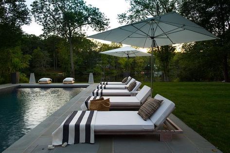 Teak pool loungers accented with white cushions sand black and white stripe towels sit on slate pavers beneath white umbrellas and facing a rectangular in ground swimming pool. Pool Patio Furniture, Pool Bed, Pool Pavers, Kerri Rosenthal, Outdoor Pool Area, Outdoor Space Design, Pool Lounger, Casa Country, Dream Pools