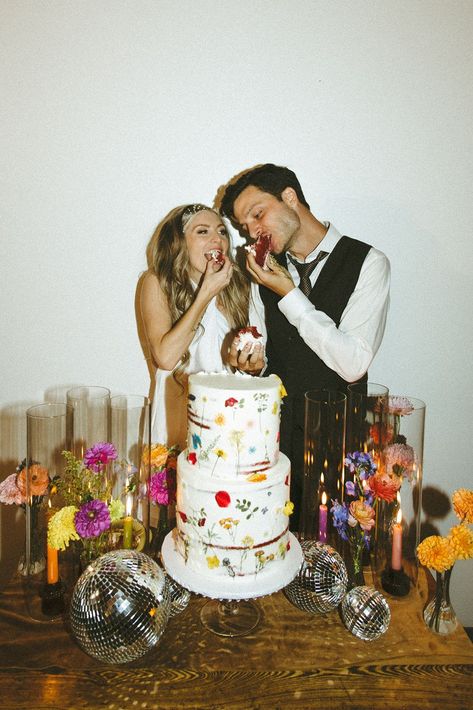 Retro & Colorful Micro-Wedding at the Doyle. Newlyweds feed eachother the wedding cake 60s Wedding Theme Vintage, Moody Retro Wedding, Retro Winter Wedding, Retro Wedding Bouquet, Eclectic Wedding Cake, 70s Wedding Photos, 70s Wedding Cake, Funky Wedding Decor, Disco Wedding Cake