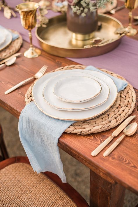 Rustic place setting with light blue linen napkin, gold flatware, & rattan placemat Farmhouse Dining Table Place Settings, Rustic Table Setting Home, Rattan Table Setting, Rattan Placemats Table Settings, Gold Flatware Table Setting, Rattan Chargers Table Setting, Napkin Placement Ideas, Dining Room Place Settings, Placemats Ideas Dining Rooms