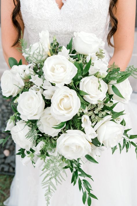 Bride in white dress holding a bouquet of white roses with greenery