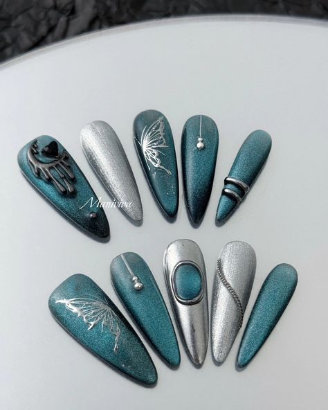 The Celestial Teal Elegance nail set exudes sophistication and mystique, featuring a stunning combination of metallic teal and silver tones. The design showcases intricate details such as a graceful silver butterfly, a dripping crescent moon embellished with a black gemstone, and delicate bead accents. The metallic finish reflects light beautifully, while silver chrome elements add a sleek, futuristic touch. Ideal for those looking to make a bold statement with their nails, this set is perfec... Futuristic Nail Designs, Chrome Teal Nails, Teal And Silver Nails, Moon Nails Design, Futuristic Elegance, Chrome Elements, Teal And Silver, Silver Nail Art, Teal Nails