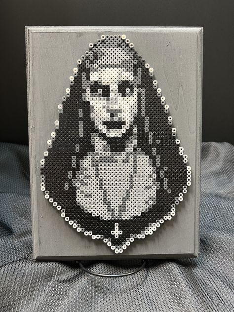 It's Valak the scary Nun from the popular Conjuring Universe horror films! Made from perler beads and mounted on a wood canvas, this creepy piece of art would look great hanging anywhere! Picture hanger included on back for easy hanging! Horror Movie Perler Bead Patterns, Hama Beads Horror, Wednesday Addams Perler Beads, Scream Perler Bead Patterns, Cross Stitch Horror, Chucky Perler Beads, Pixel Art Creepy, Scream Perler Beads, Scary Pixel Art