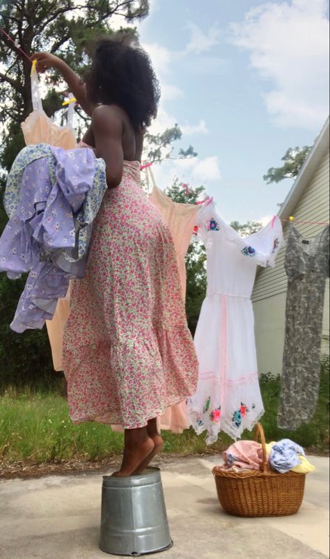 cottagecore black girl drying laundry on a clothesline with a washboard and basket, standing on a bucket. aesthetic, black girl, soft life, vision board, floral halter dress, wattpad, main character, bw, farm girl, blue sky, dresses, basket, natural hair, curly girl, vintage, cottage, poc cottagecore Aesthetic Laundry, Poc Cottagecore, Black Cottagecore, Cottagecore Princess, Bodycon Short Dress, Laundry Clothesline, Life Vision, Short Bodycon Dress, Dresses Aesthetic