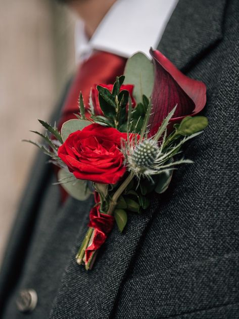 A close up of a deep red floral buttonhole. Pinned to a man's suit. Velvet Ribbon Wedding Bouquet, Red Fall Bouquet, Red Rose And Thistle Bouquet, Christmas Wedding Buttonholes, Lilly Bouquet Wedding, Thistle Buttonhole, Buttonholes Wedding, Red Rose Boutonniere, Velvet Ribbon Wedding