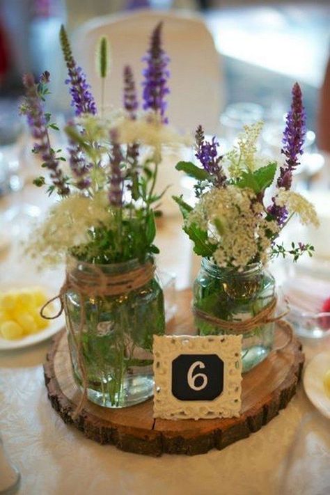 a wood slice with two mason jars with wildflowers and a lace table number for a rustic wedding Flower Table Numbers, Spring Mason Jar, Wedding Centerpieces Mason Jars, Table Centerpieces Diy, Fall Mason Jars, Table Arrangements Wedding, Vintage Mason Jars, Mason Jar Flowers, Rustic Mason Jars