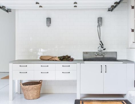 Transitional white garage with white flat front cabinets featuring concrete countertops and a utility sink. Garage Sink, Stone Cottage Homes, Grey Garage Doors, Above Garage Apartment, Flat Front Cabinets, Garage Utility, Herringbone Tile Backsplash, Traditional Light Fixtures, White Siding