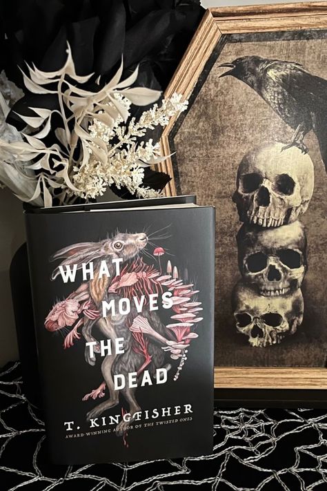 Bookish photo of What Moves The Dead by T. Kingfisher in front of spooky halloween decor like a print with skulls and a raven and a spiderweb table runner. What Moves The Dead, T Kingfisher, Book Club Reads, Book Recommendation, Horror Novel, Horror Book, Novels To Read, Gothic Horror, Kingfisher