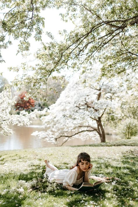 Brunette girl in long white dress lies in the grass surrounded by cherry blossom petals, reading an antique book Botanical Garden Photo Shoot, City Fashion Photography, Regency Romance, Outdoor Photoshoot, Senior Photoshoot, Garden Photography, Spring Photography, Photoshoot Concept, Garden Photos