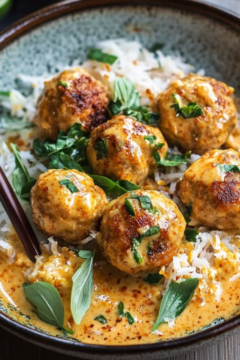 A bowl of coconut chicken meatballs served over a bed of white rice, topped with fresh cilantro. The golden-brown meatballs are nestled in a rich, creamy coconut curry sauce, with visible red chili peppers adding a pop of color. The dish is vibrant and hearty, presenting a delicious blend of savory and aromatic flavors. Coconut Meatball Curry, Keto Thai Meatballs, Middle Eastern Chicken Meatballs, Thai Chicken Meatball Curry, Chicken Pork Meatballs, Coconut Chicken Meatballs, Thai Chicken Balls, Thai Coconut Meatballs, Thai Pork Meatballs