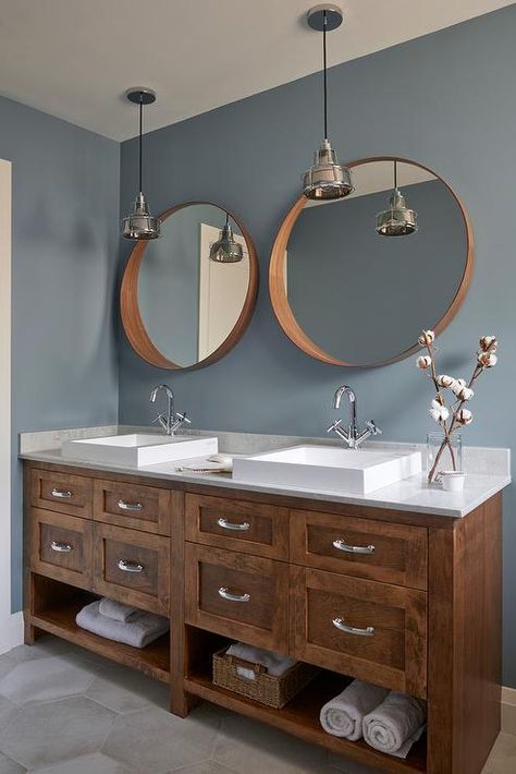 Wonderfully designed blue and brown bathroom boasts brown convex mirrors hung from a blue wall above a brown oak dual washstand fitted with towel shelves and polished nickel pulls and placed on large gray hex floor tiles. Towel Shelves, Blue And Brown Bathroom, Gray Hex, Bathroom Wall Colors, Ideas Cuarto, Brown Bathroom Ideas, Brown Floors, Transitional Bathroom, Brown Bathroom