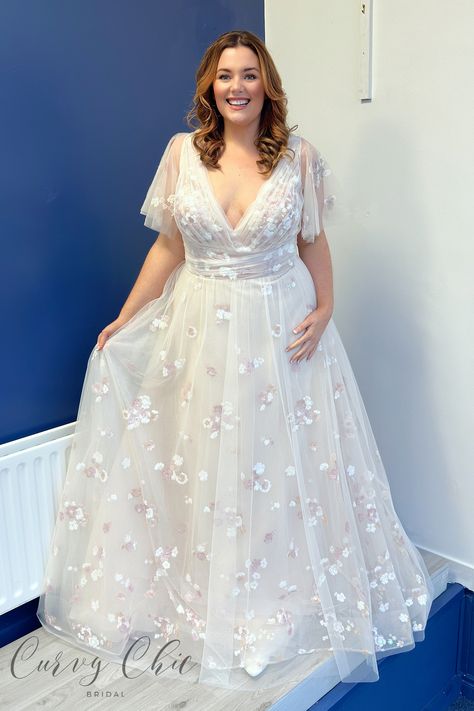 <p>Introducing Gracie, a dreamy plus-size wedding dress that exudes soft romance.</p> <p>Layers of tulle with blush floral sequin detail create an enchanting A-line silhouette. The structured V-neckline and draped bodice gracefully lead to a low back adorned with delicate pearl buttons. Complete with flutter sleeves, Gracie offers various sleeve options and customisations for a uniquely personalised touch. This gown is a perfect blend of whimsy and elegance, ensuring a captivating and unforgettable bridal look.</p> <p> </p> <p>Customisation options available</p> <p class="p1">Sizes: 12, 14, 16,18,20,22,24 and up (no upper limit!)</p> <p class="p1">Have a question about Gracie by Rebecca James Bridal? Just get in touch – <a href="https://www.curvychicbridal.com/contact/"><span cl