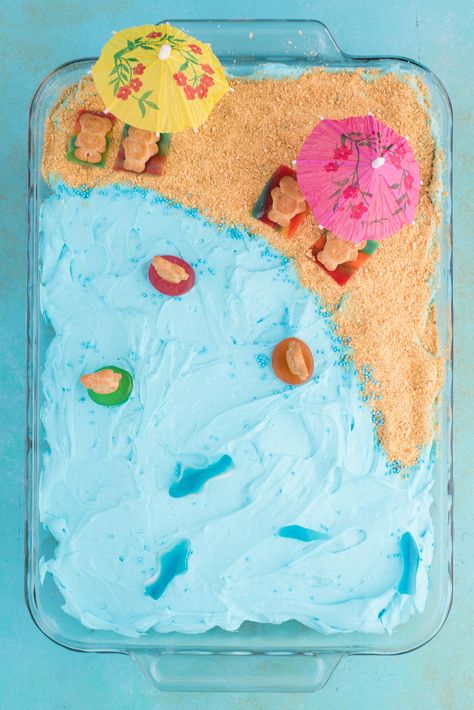 This beach theme poke cake would be a hit at a beach theme party or under the sea theme party! Kids will have fun decorating the top of this beach cake with teddy grahams, gummy sea creatures, and graham cracker sand. #beachpokecake #pokecake #beachcake Diy Beach Cake Birthday, Third Birthday Beach Theme, Beachy Birthday Cake Ideas, Diy Ocean Cake, Beach Cake With Jello, Beach Scene Cake, Easy Beach Theme Cake, Simple Ocean Theme Cake, Beach Theam Birthday Party