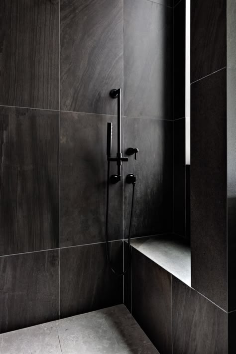 The couple’s bathroom shower is a moody alcove covered with deep black Emilceramica porcelain tile. Dark Brizo shower fixtures enhance the drama. Noir Veined Tile Bathroom, Black Large Tile Bathroom, Dark Tile Shower Ideas Small Bathrooms, Black Walk In Shower Ideas Tile, Shower Tile Ideas Black, Dark Tile Bathroom Ideas, Dark Tiles In Bathroom, Dark Bathroom Tile Ideas, Dark Gray Bathroom Tile