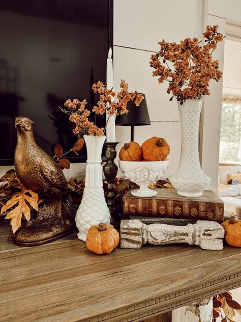 White milk glass bud vase for fall mantel decorations.  a pheasant and orange pumpkins with old books. Vintage Fall Centerpieces, Pheasant Fall Decor, Brandy Snifter Decor Ideas, Clear Glass Pumpkin Decor, Decorating With Milk Glass Ideas Fall, Milk Glass Vase Display, Milk Glass Fall Decor, Vintage Mantel Decor, Fall Booth Ideas